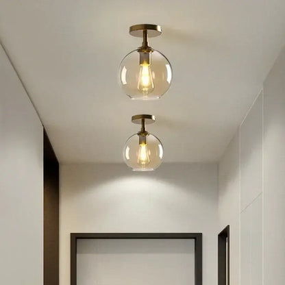 Two brass-finished globe glass pendant lights with clear shades and filament bulbs for dining room use