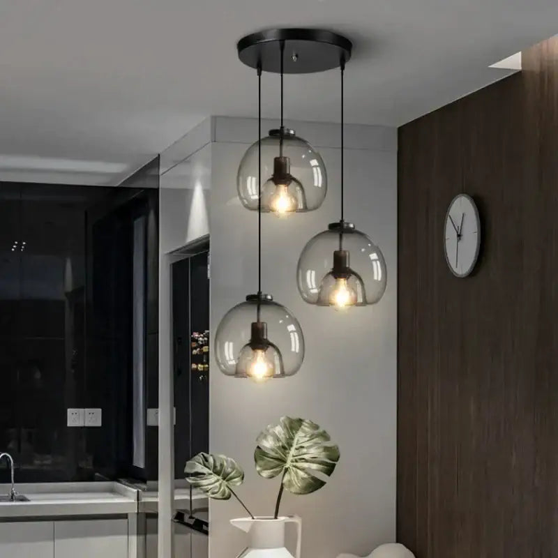 Set of three smoked glass pendant lights with black metal fixtures and warm glowing bulbs for dining room use