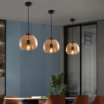 Three amber-tinted smoked glass pendant lights with black metal fixtures hang above a dining table centerpiece