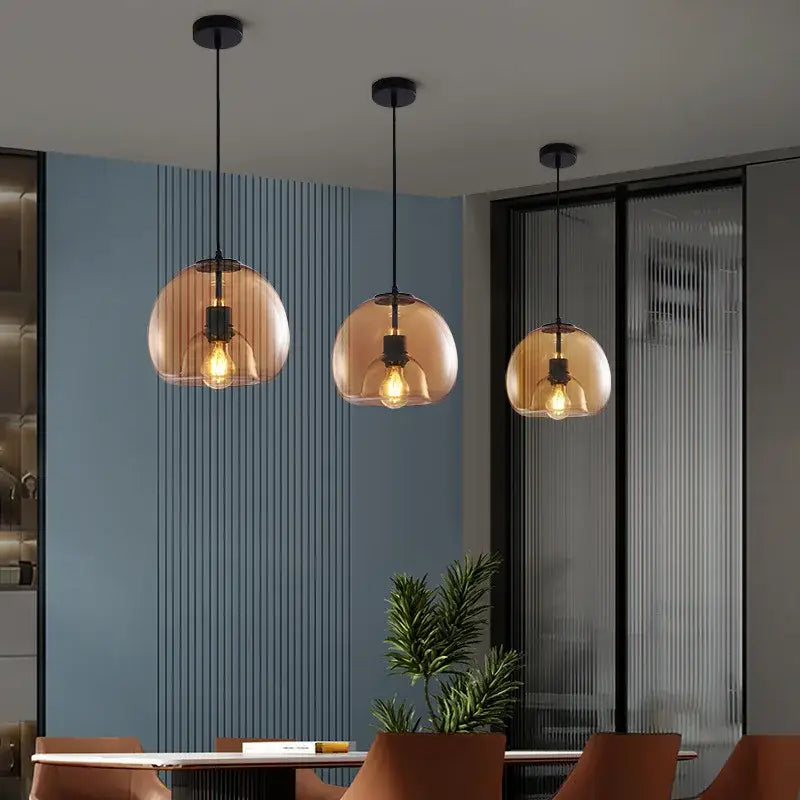 Three amber-tinted smoked glass pendant lights with black metal fixtures hang above a dining table centerpiece