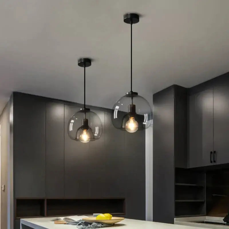 Two modern smoked glass pendant lights with clear globe shades and exposed filament bulbs for dining table use