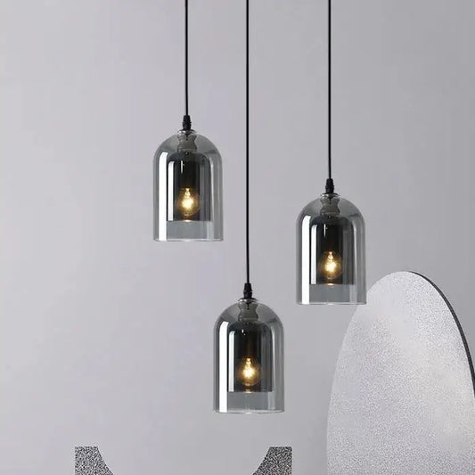 Three sleek smoky gray glass pendant lights with black cords and exposed filament bulbs for dining room use