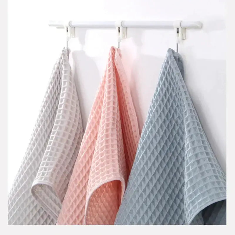 Three soft gray blush and blue cotton waffle towels hang on a white rack in this decorbites cotton waffle towel bath set