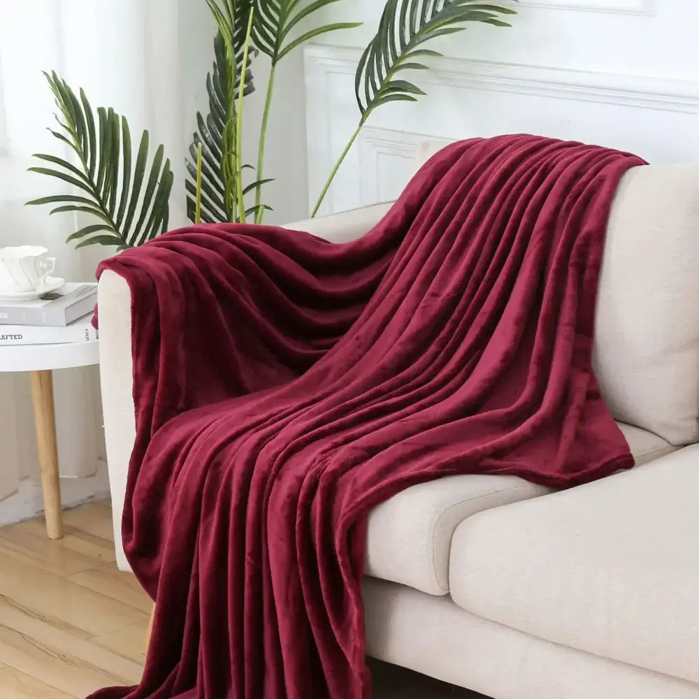 A plush deep burgundy decorbites cozy flannel throw blanket with soft velvety texture draped over a beige sofa