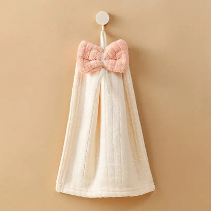 A soft off-white decorbites bowknot microfiber hand towel with a plush pink bow hangs from a hook for kitchen and bathroom
