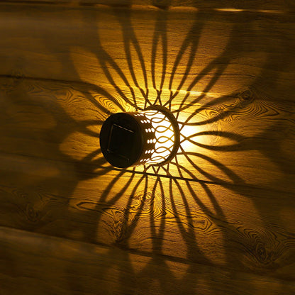 Black solar-powered datura lantern with intricate cut-out patterns casting sunburst shadows on wooden surface for outdoor garden decor