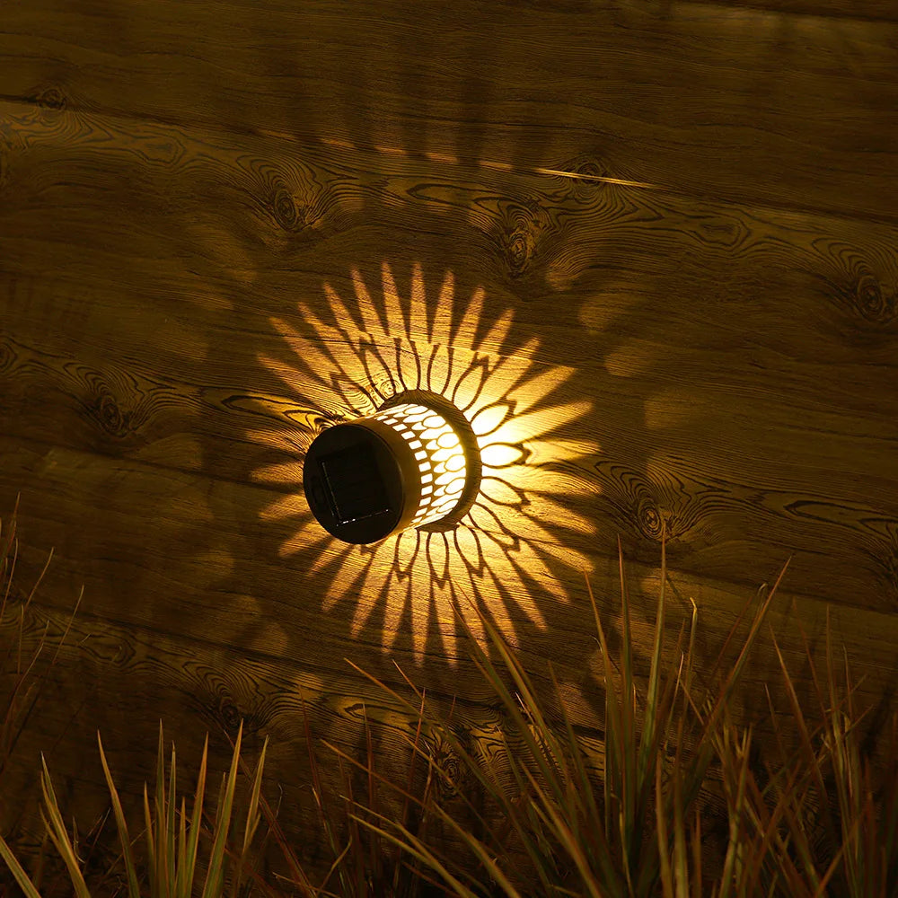 Solar-powered datura lantern wall lamp with sunburst design and warm yellow light casting decorative shadows on wood