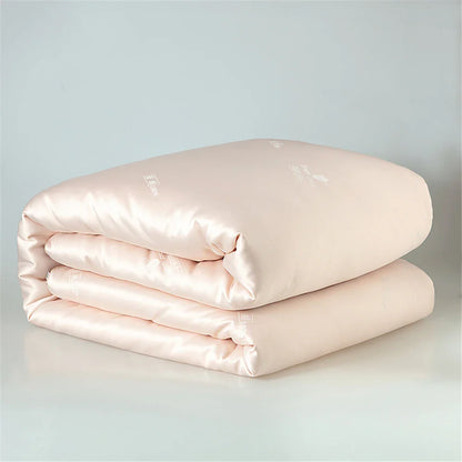 A soft blush pink satin silk quilt with subtle sheen and delicate embroidered branding for luxurious sleep
