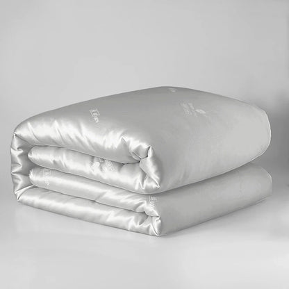 A sleek silver satin-finish sondeson luxury natural 100% silk quilt with subtle embroidered branding for sleep comfort