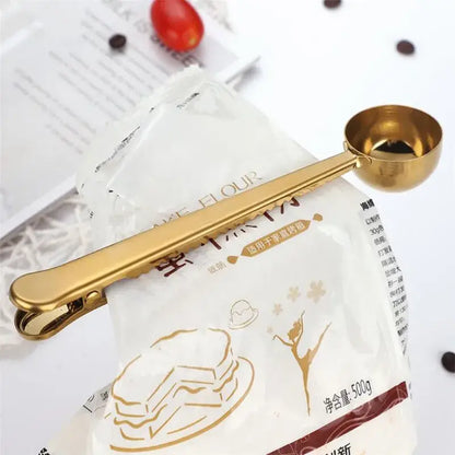 Gold-colored stainless steel coffee spoon with sealing clip designed for precise portioning of dry ingredients
