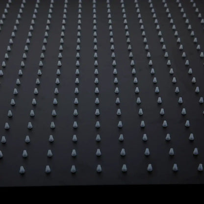 Rows of uniform white plastic spikes on the back side of a super slim matte black square rain shower head fixture