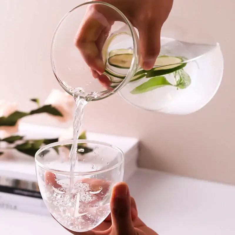 Clear teal hourglass glass tea infuser water bottle pouring cucumber mint water into matching glass carafe
