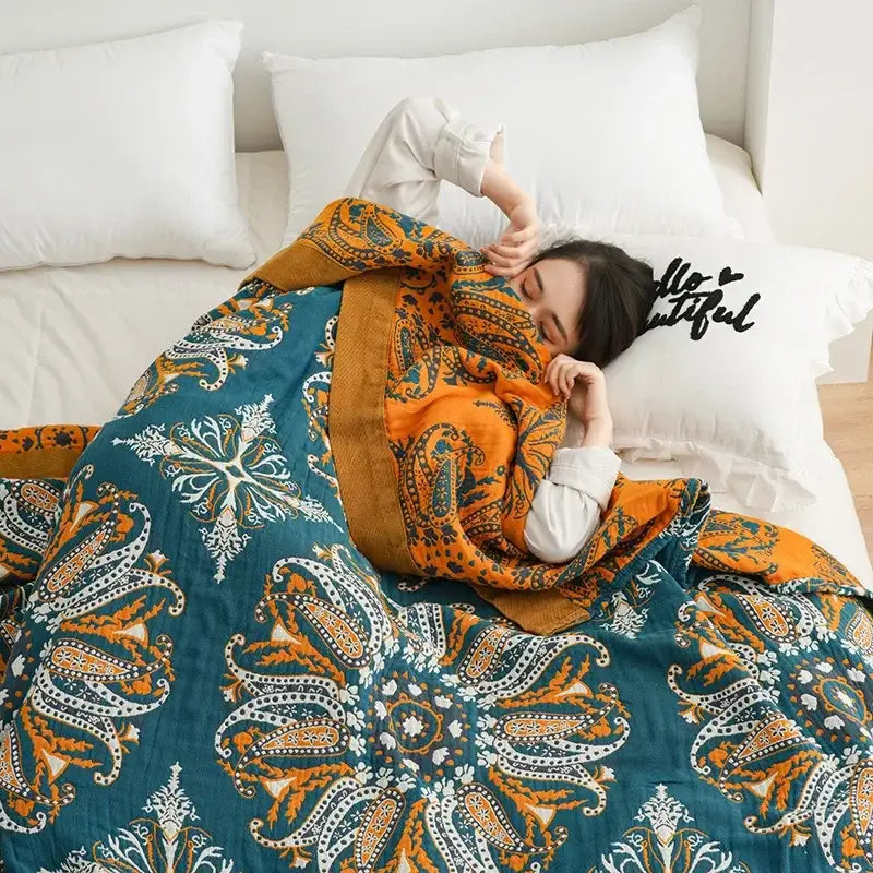 A cozy teal and orange paisley-patterned geometric cotton gauze summer blanket draped over a sleeping person