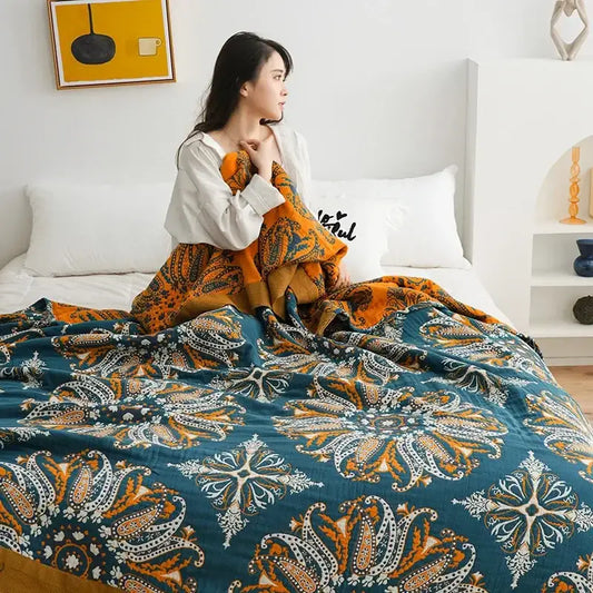 A cozy teal and orange paisley decorbites geometric cotton gauze summer blanket draped over a woman in bed
