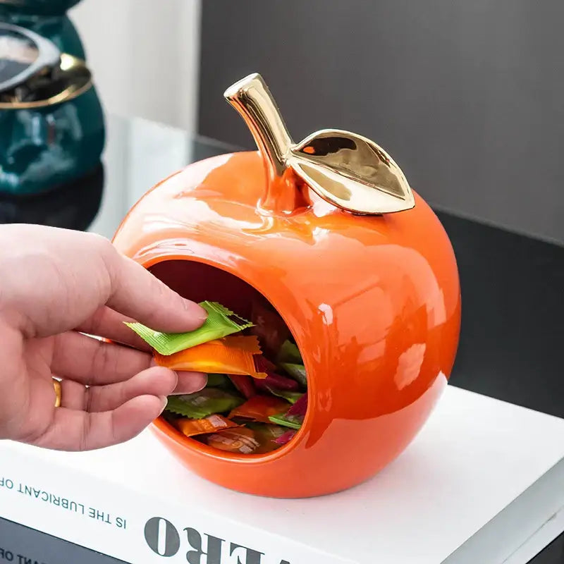 Vibrant orange ceramic apple storage box with glossy finish and gold toned stem for living room storage box use