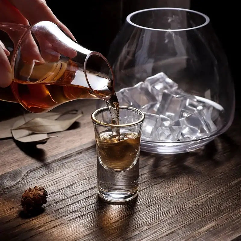 A clear glass wine pot shot glass with gold rim filled with amber liquid for dining room and bar use