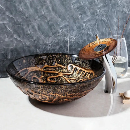 Glossy black glass wash basin set with intricate gold leaf patterns and matching bronze waterfall faucet for bathroom