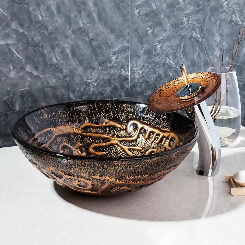 Textured black and gold glass wash basin set featuring a glossy vessel sink with gold leaf patterns and bronze faucet