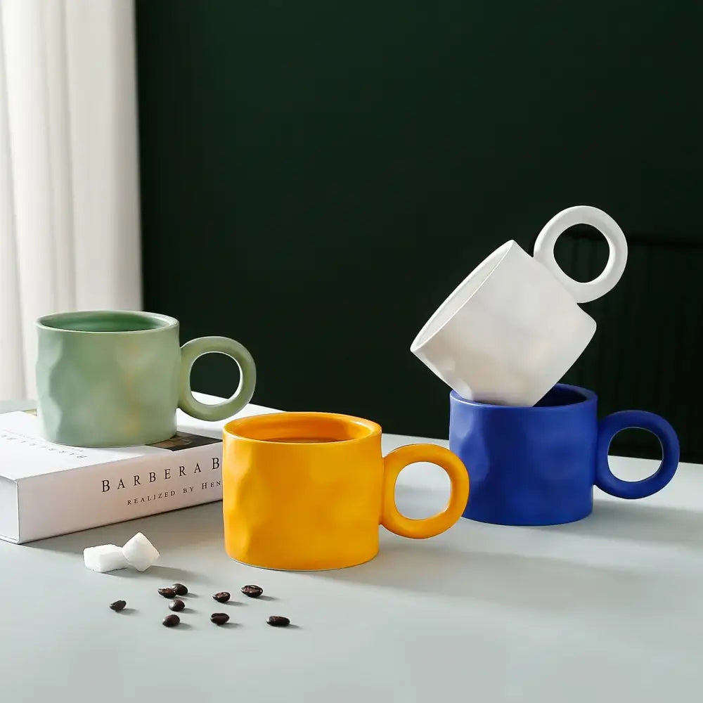 A set of four ceramic coffee mugs in vibrant green yellow blue and white with textured matte finish and round handles