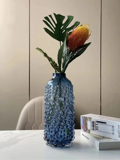 Translucent blue textured glass flower vase with raised bubbles holding monstera leaves and orange flower for decorbites clear glass decor