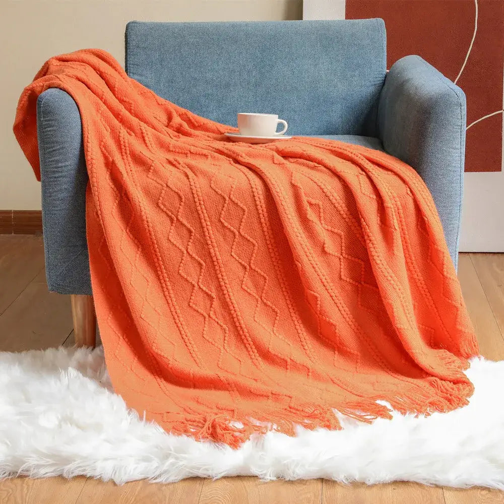Vibrant orange textured diamond knit throw blanket with fringed edges draped over blue armchair decorbites cozy knit