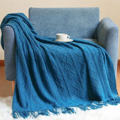 A cozy teal cable knit throw blanket with fringed edges draped over a blue armchair perfect for decorbites cozy knit decor