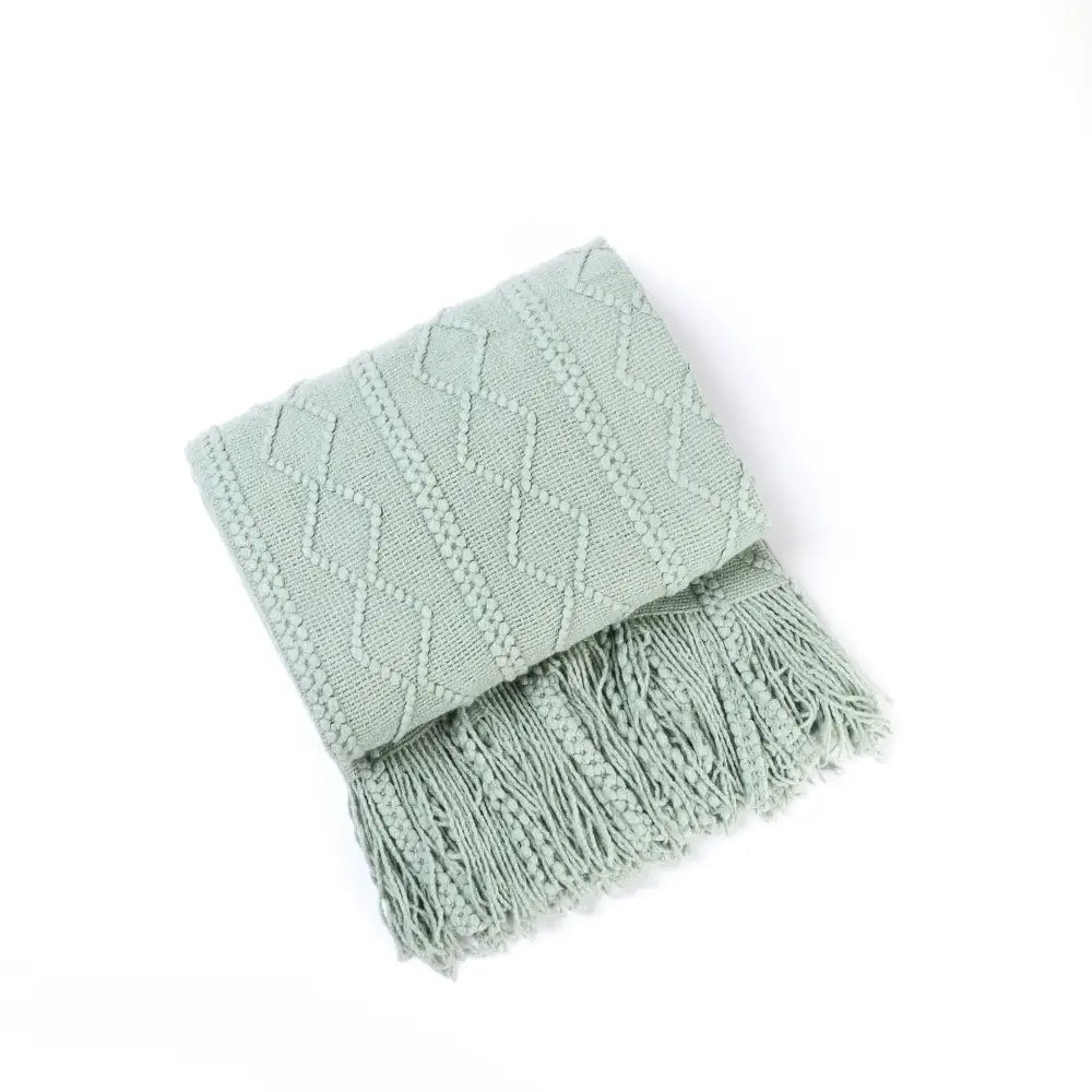 A soft mint green knit throw blanket with a textured diamond pattern and fringed edges perfect for cozy knit decorbites decor