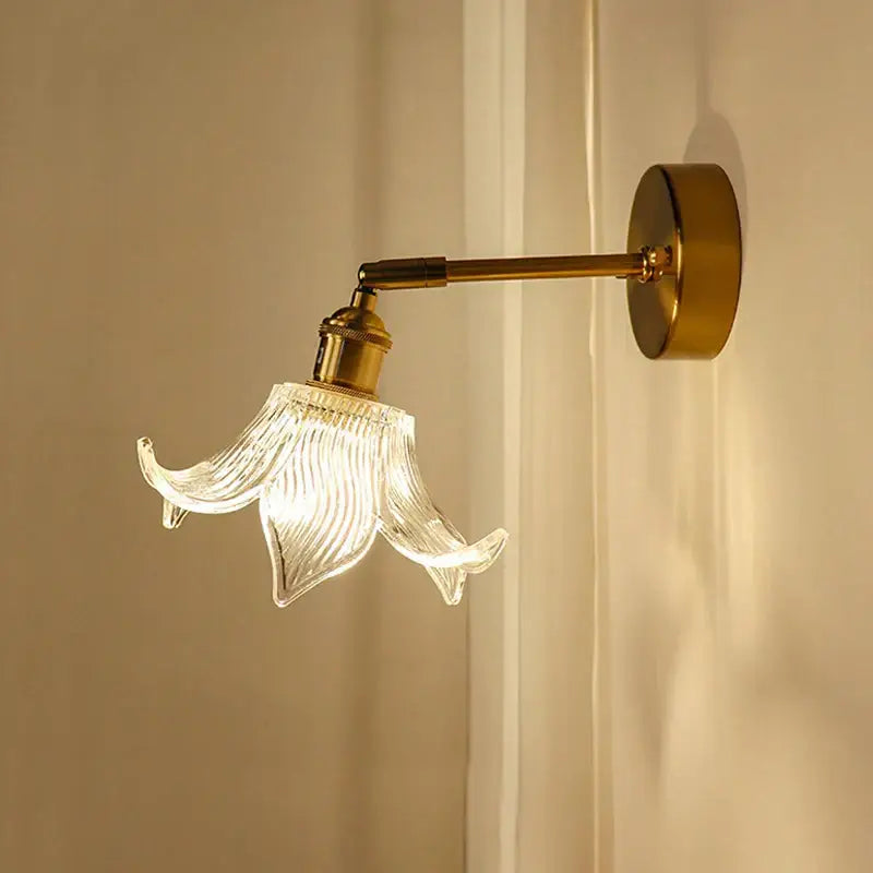 Delicate gold-toned wall sconce with open flower ribbed glass shade featuring decorbites brass mirror design for bedroom