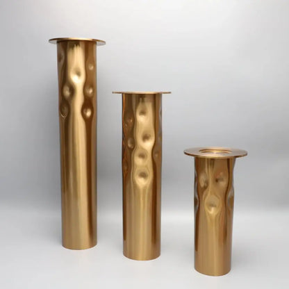 Set of three brass-colored textured golden metal candlestick holders with hammered surface and flared rims for decorbites