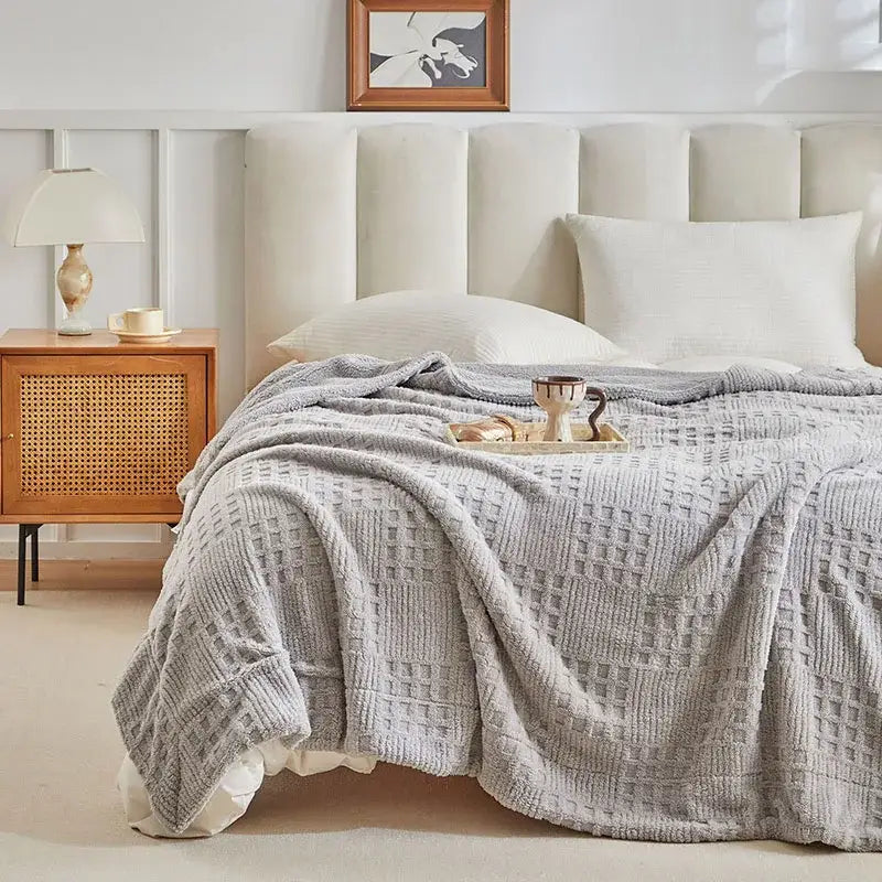 A soft textured gray coral fleece blanket with a subtle woven pattern draped over the bed as a knit throw