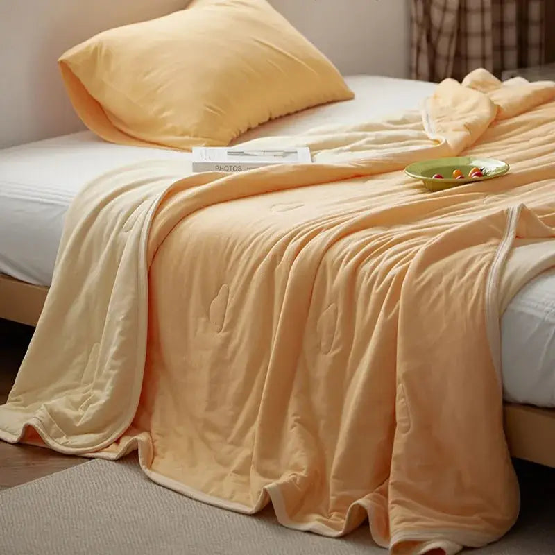 Soft peach-colored quilted decorbites cotton summer comforter with subtle texture draped over a bed for cooling comfort