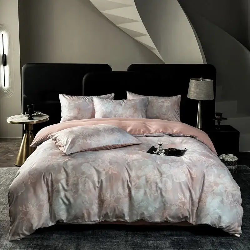 A luxurious blush pink and silver floral satin bedding set with matching pillowcases draped over a black bed frame