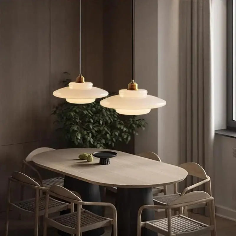 Two elegant off-white glass pendant lights with brass accents hang above a dining table in cream tiered design