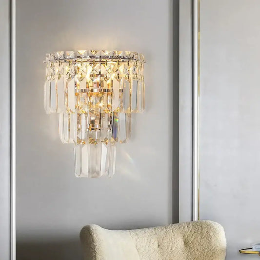 A tiered gold crystal wall lamp with clear faceted glass prisms and polished metal frame for elegant decorbites crystal wall decor