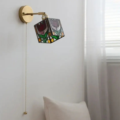 A brass-finished wall light with a colorful square glass shade featuring floral designs for decorbites colorful square lighting