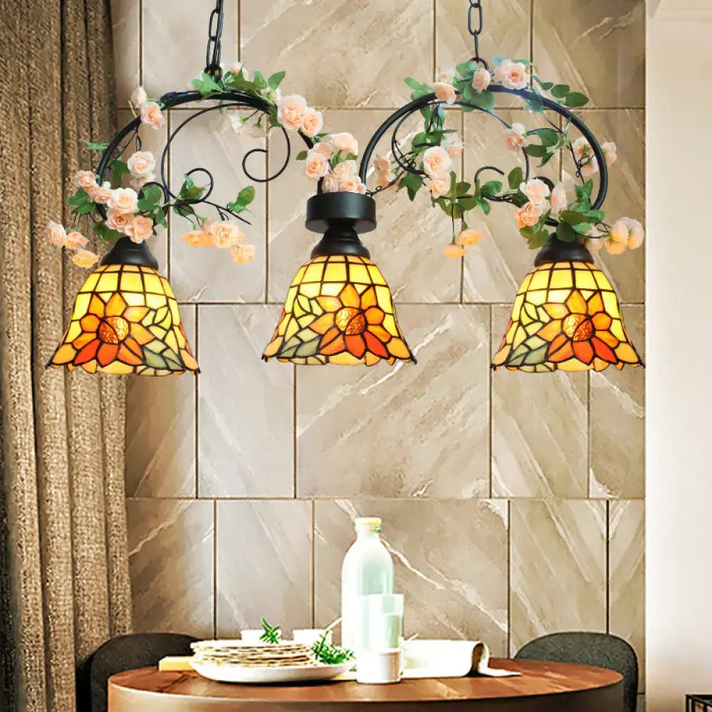 Three-piece tiffany-style pendant light with art glass sunflower shades and black wrought iron frame adorned with pink roses