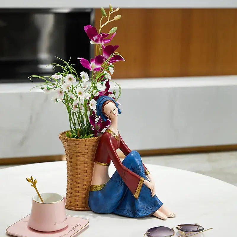 A ceramic resin ornament of a woman in a blue and red dress with gold trim beside a basket of purple flowers for cute girls storage