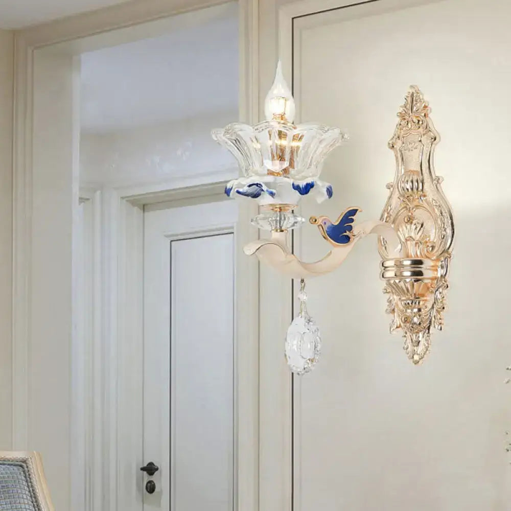 Elegant gold-toned brass wall sconce light with clear glass flower design blue bird motif and dangling crystal teardrop