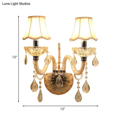 Traditional gold crystal wall sconce with two ornate arms, fabric shades, and dangling teardrop crystals for bedroom lighting