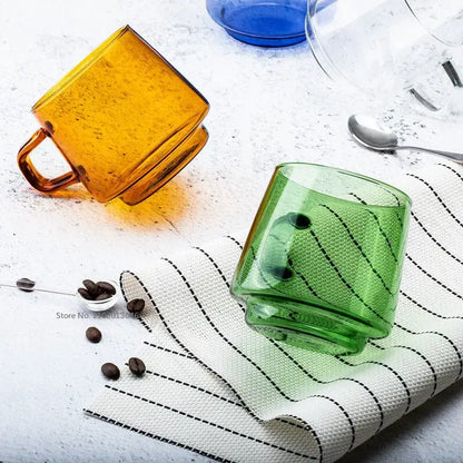 Translucent green glass coffee mug with textured surface and black accents resting on a striped cloth