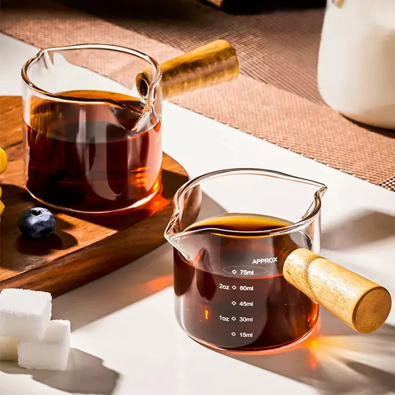 Transparent glass espresso measuring cups with wood handle filled with dark amber liquid for precise measuring