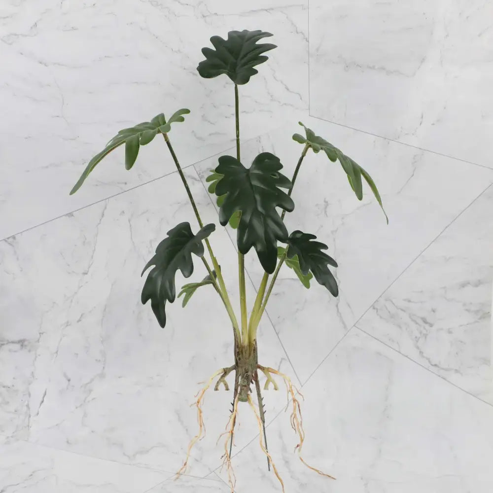 Artificial green philodendron plant with glossy lobed leaves and visible roots in tropical plant wall set for living room decor
