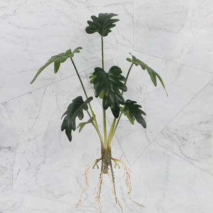 Artificial green philodendron plant with glossy lobed leaves and visible roots in tropical plant wall set for living room decor