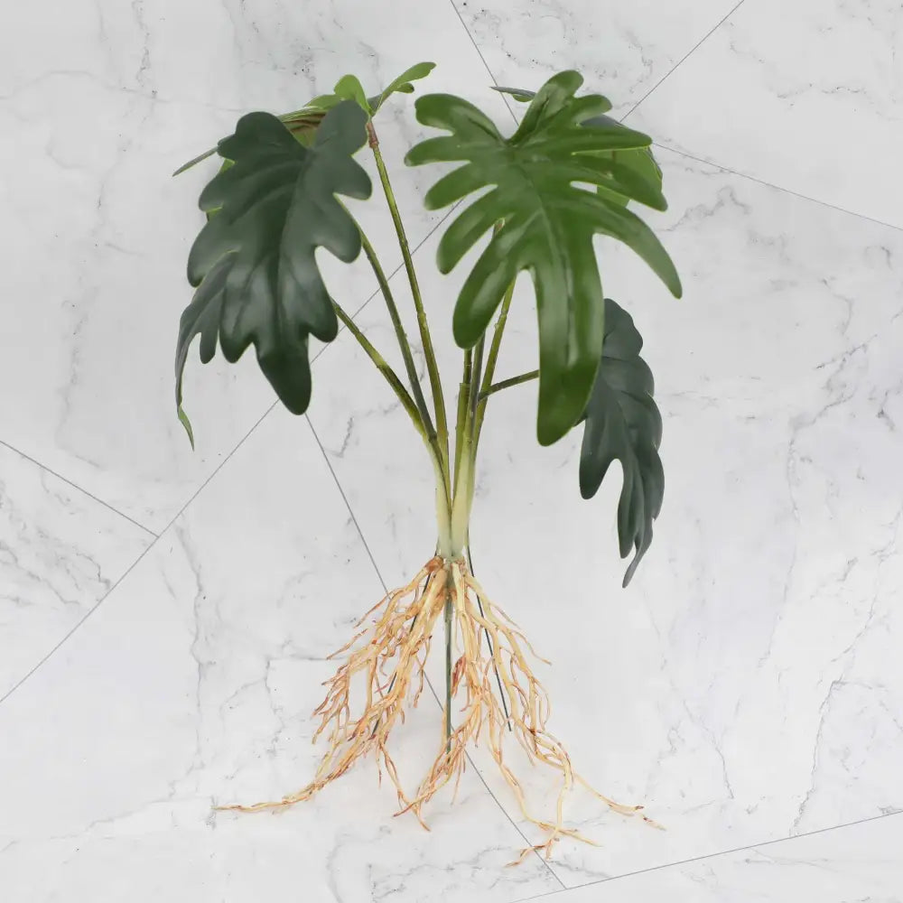Artificial green monstera plant with glossy leaves and tan roots in tropical plant wall set for living room decor