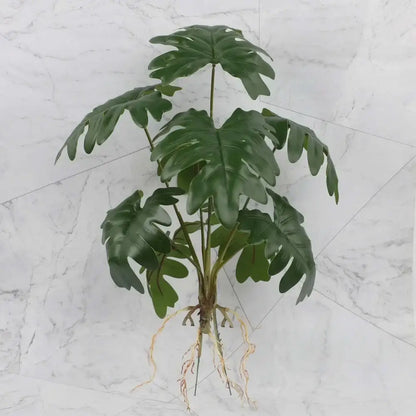 Artificial green monstera plant with glossy deeply lobed leaves and visible roots in tropical plant wall set for living room decor