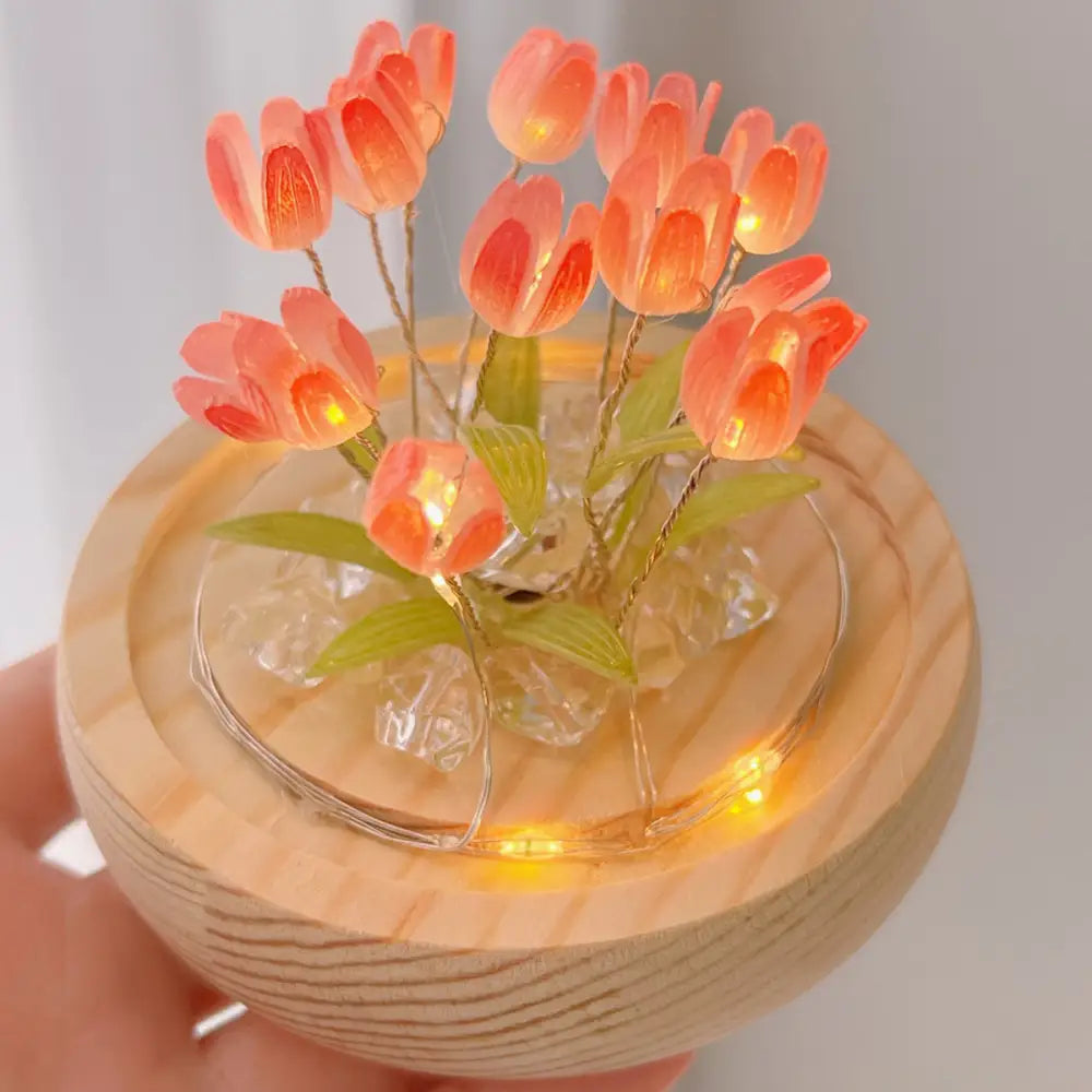 A delicate peach-colored translucent tulip night light with glowing orange interiors on a wooden base with glass beads