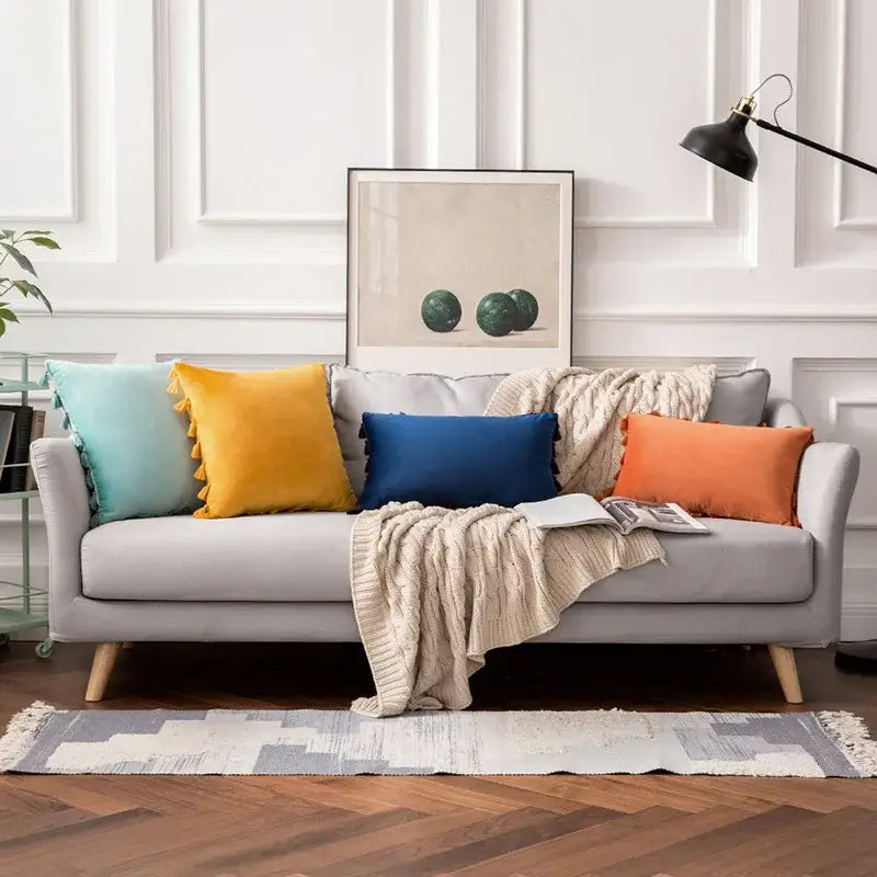 Gray upholstered sofa with wooden legs featuring vibrant decorbites fringed tassel velvet colorful throw pillows