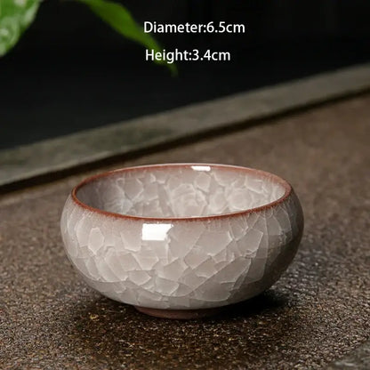 A small handcrafted ceramic tea bowl with soft gray and brown tones featuring decorbites ice cracking glaze design