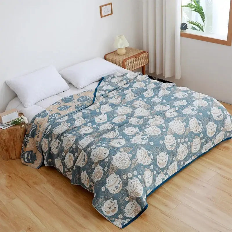 A soft teal nordic throw blanket with cream lucky cat patterns and floral accents complements an orange gold bedspread