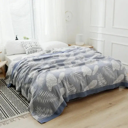 Gray throw blanket with white leaf patterns and blue border paired with vibrant orange and gold geometric nordic throw blanket